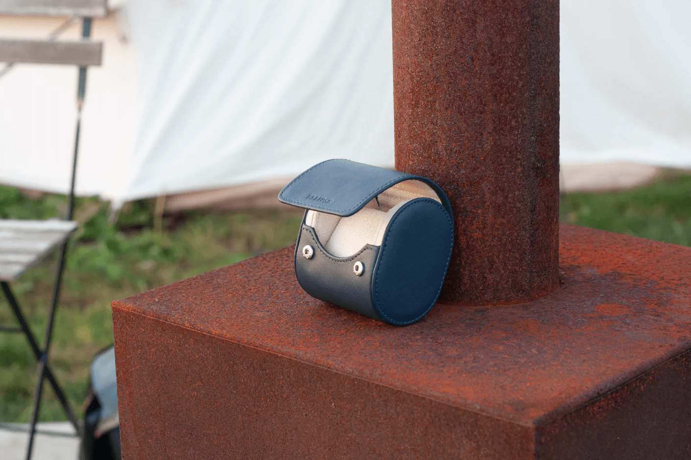 Elevate your watch collection's safety and style with our exquisite Luxury Watch Travel Roll. Crafted in striking Midnight Navy Blue and featuring a lavish Cream Microfiber Interior, this travel essential blends elegance and protection seamlessly. In this captivating image, our watch roll rests gracefully beside a weathered chiminea furnace, bathed in the warm hues of a picturesque sunset. Nearby, a charming bell tent and inviting garden chair invite you to embark on a journey of luxury. Explore this premium travel accessory and safeguard your watches in unparalleled sophistication.